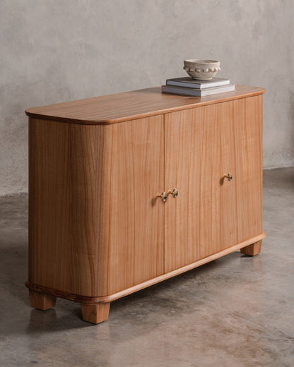 Wooden sideboard console with 3 doors against a grey wall.